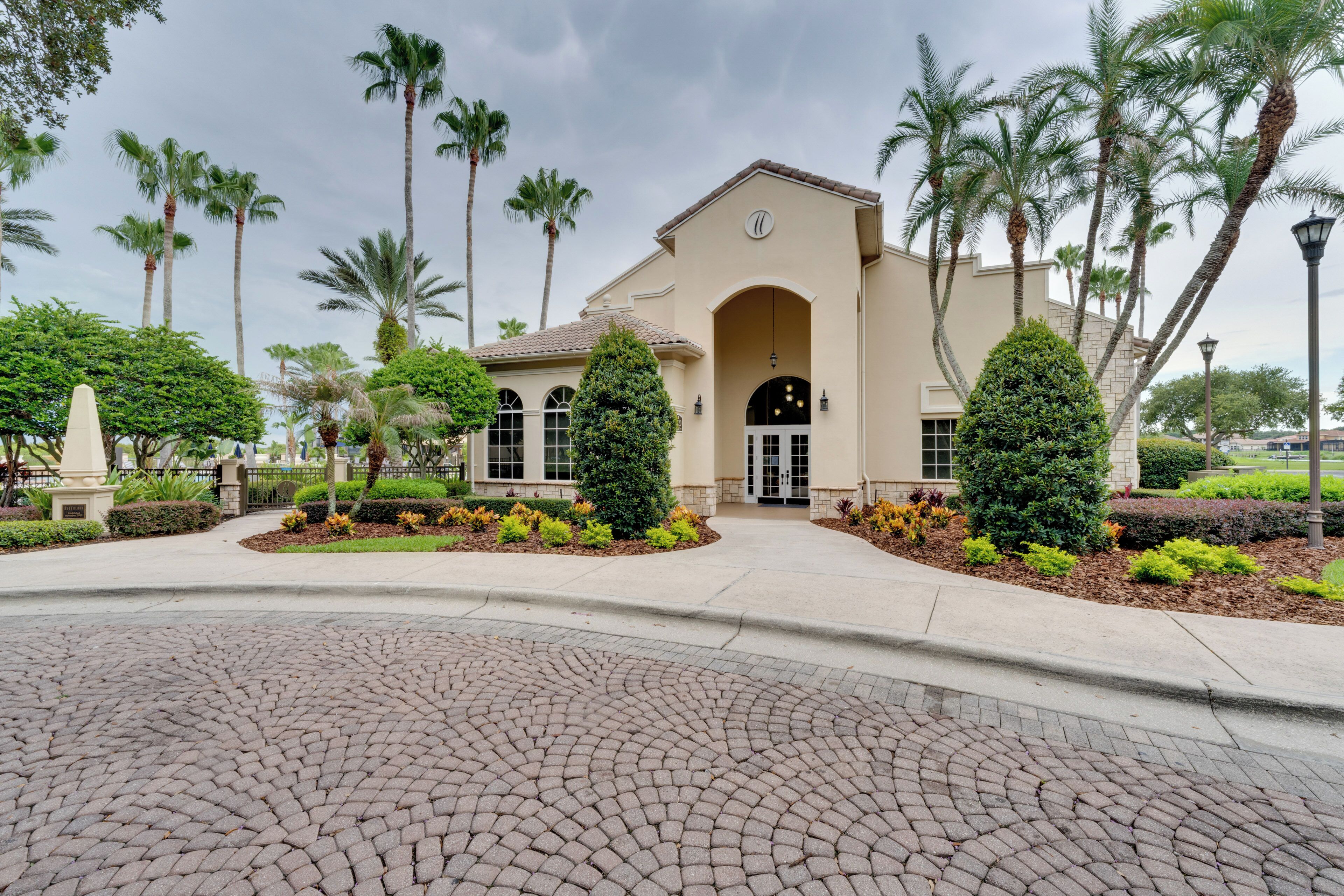 A building with a central arched entrance, surrounded by a landscaped garden with palm trees and shrubs.