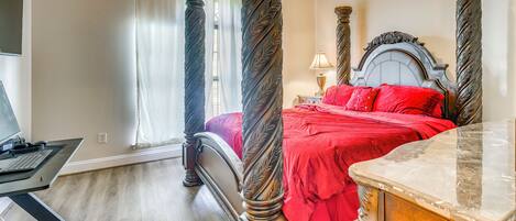 A bedroom with a four-poster bed, a desk with a computer, and a marble side table.