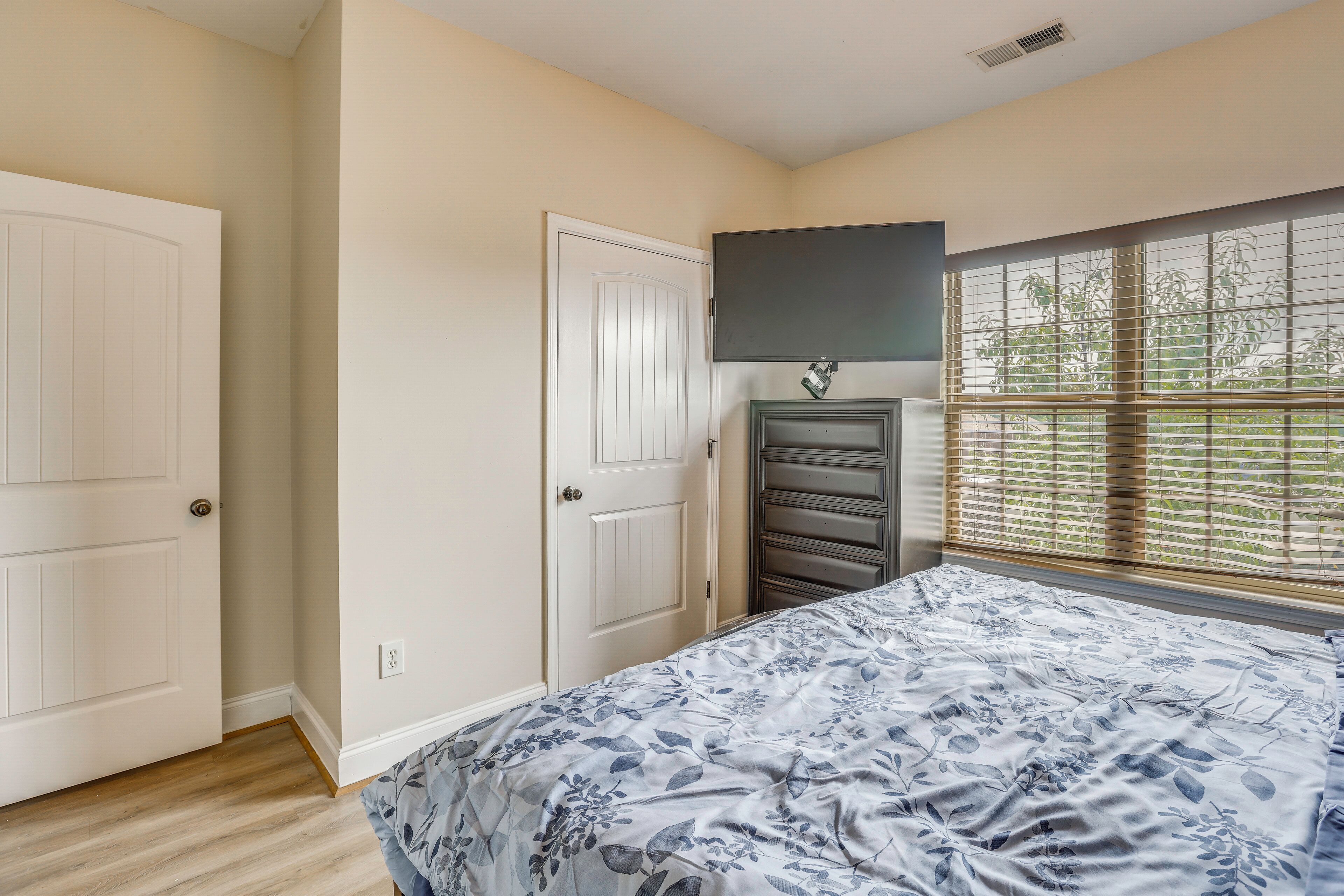 Un dormitorio con cama, televisor montado en la pared y ventana con persianas.