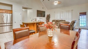 A spacious dining area with a wooden table and chairs, a kitchen with stainless steel appliances, and a living area with a sofa and a decorative plant.