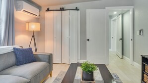 A modern living room with a sofa, a floor lamp, a potted plant, and a sliding door closet. - Work & Relax in Safety Harbor! Modern Coastal Apt (Safety Harbor)