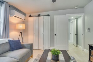 A modern living room with a sofa, a floor lamp, a potted plant, and a sliding door closet. - Work & Relax in Safety Harbor! Modern Coastal Apt (Safety Harbor)