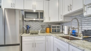 A modern kitchen with white cabinets, stainless steel appliances, and a marble countertop. - Work & Relax in Safety Harbor! Modern Coastal Apt (Safety Harbor)