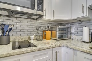 A kitchen with white cabinets, a stainless steel range hood, a microwave, a double oven, and a marble countertop. - Work & Relax in Safety Harbor! Modern Coastal Apt (Safety Harbor)