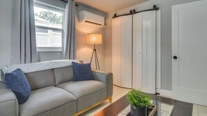 A modern living room with a sofa, a lamp, a potted plant, and a sliding door. - Work & Relax in Safety Harbor! Modern Coastal Apt (Safety Harbor)