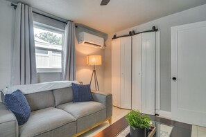 A modern living room with a sofa, a lamp, a potted plant, and a sliding door. - Work & Relax in Safety Harbor! Modern Coastal Apt (Safety Harbor)