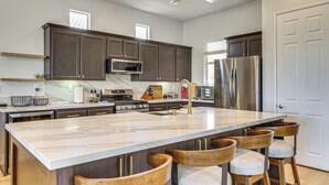 A modern kitchen with dark wood cabinets, stainless steel appliances, a marble island, and bar stools. - Indian Palms Retreat Across From Empire Polo Club (Indio)