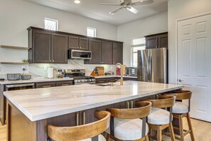 A modern kitchen with dark wood cabinets, stainless steel appliances, a marble island, and bar stools. - Indian Palms Retreat Across From Empire Polo Club (Indio)