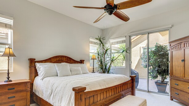 A bedroom with a wooden bed, a nightstand, a lamp, a ceiling fan, and a view through a sliding glass door. - Indian Palms Retreat Across From Empire Polo Club (Indio)
