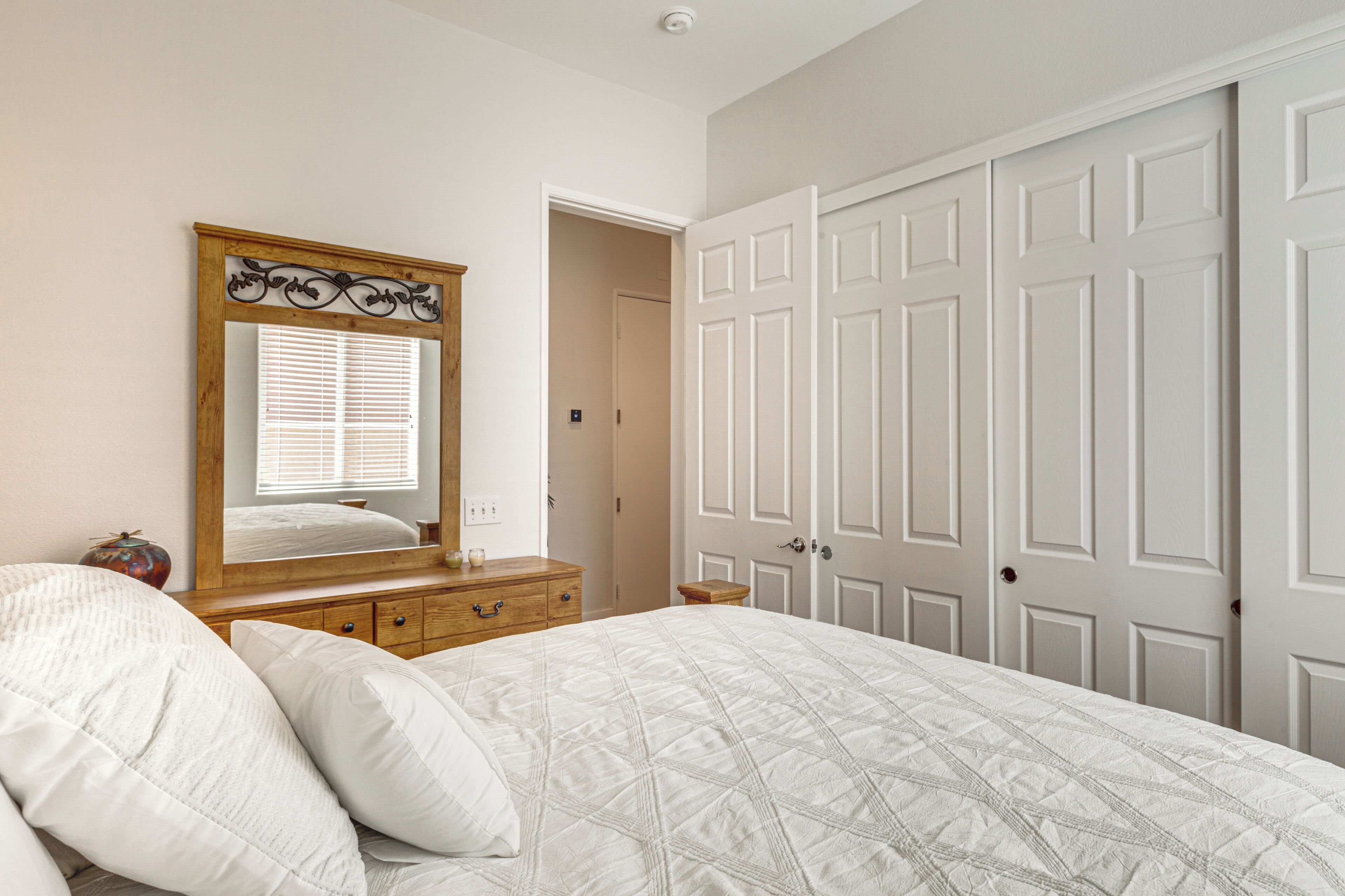 Een slaapkamer met een bed, een dressoir, een spiegel en een kledingkast.