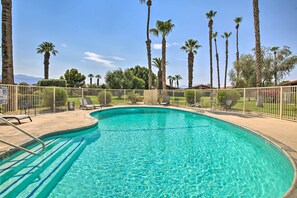 A clear blue swimming pool surrounded by a white fence, with palm trees and a clear sky in the background. - Indian Palms Retreat Across From Empire Polo Club (Indio)