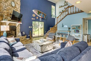 A living room with a stone wall, a television, a fireplace, a large window, a staircase, and a bookshelf.