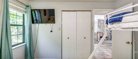 A room with bunk beds, a door, a window with curtains, and a television on the wall.