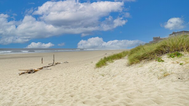 A beach with sand dunes, a wooden post, and a building in the distance. - Walk to Beaches! Lincoln City Family Home w/ Yard (Lincoln City)