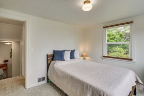 A bedroom with a bed, a window, a nightstand, and a door leading to another room. - Walk to Beaches! Lincoln City Family Home w/ Yard (Lincoln City)