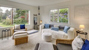 A cozy living room with a sofa, two armchairs, a coffee table, and a side table with a lamp. There are two windows offering a view of greenery outside. - Walk to Beaches! Lincoln City Family Home w/ Yard (Lincoln City)