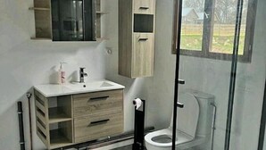 A bathroom with a wooden cabinet, a white sink, a toilet, and a glass shower enclosure. - Equi Lodge Mer: A Horse-Loving Retreat Near Disney (La Houssaye-en-Brie)