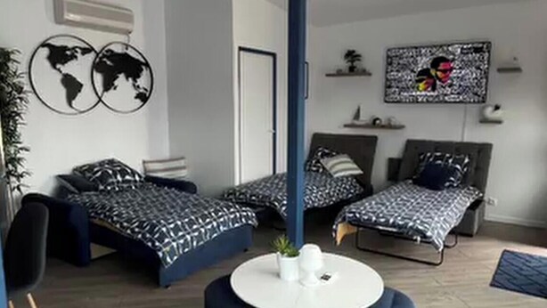 A modern bedroom with two beds, a round white table, and blue ottomans. - Equi Lodge Mer: A Horse-Loving Retreat Near Disney (La Houssaye-en-Brie)