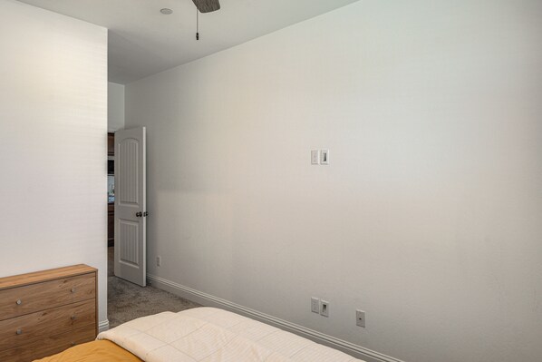 A bedroom with a wooden dresser, a bed with a white comforter, and a door leading to a bathroom.