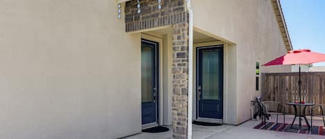 Una casa con patio cubierto, dos puertas y un pequeño espacio exterior con mesa y sillas.