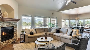 Uma sala de estar moderna com lareira, um sofá seccional, uma mesa de centro e um espaço de jantar com vista para montanhas.
