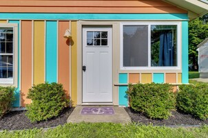 Una casa colorida con una puerta blanca, una ventana con cortina y un felpudo.
