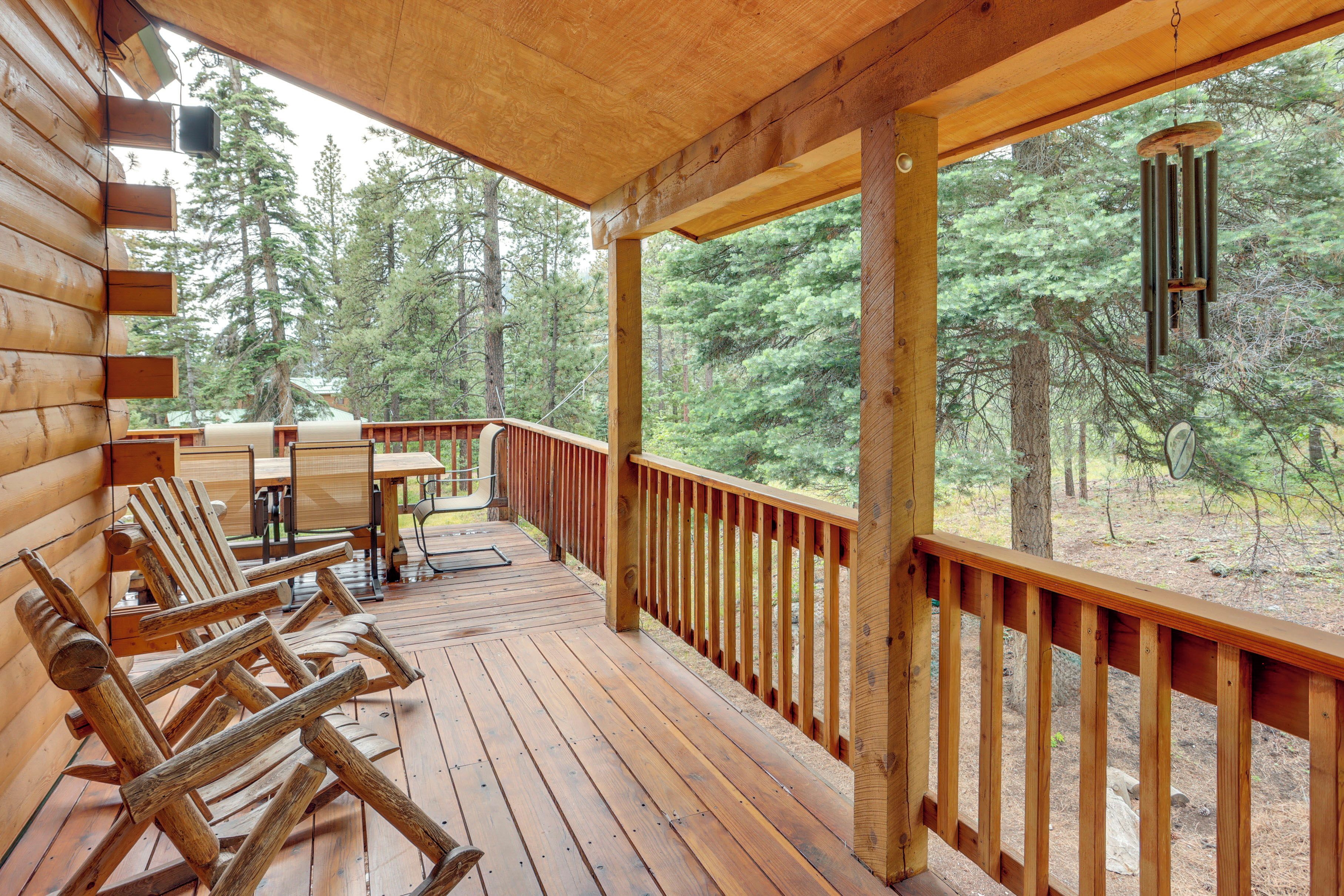 A wooden deck with outdoor seating and a view of a forest.