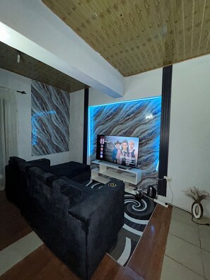 Un soggiorno moderno con un divano componibile, una televisione a schermo piatto e una parete decorata con motivi marmorei.