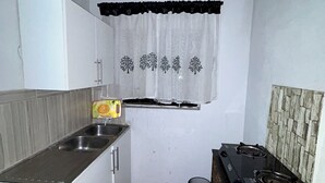 Ett kompakt kök med vita skåp, en diskho, en spis och ett fönster med gardin.