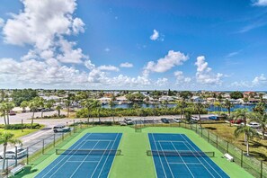 A tennis court with two courts, surrounded by a fence, with a view of a residential area and water body in the background. - Pool, Pickleball & Beach! Gulf Island Club Condo (Hudson)