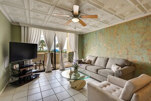 A living room with a flat-screen TV, a glass coffee table, a beige sofa, and a ceiling fan. - Pool, Pickleball & Beach! Gulf Island Club Condo (Hudson)