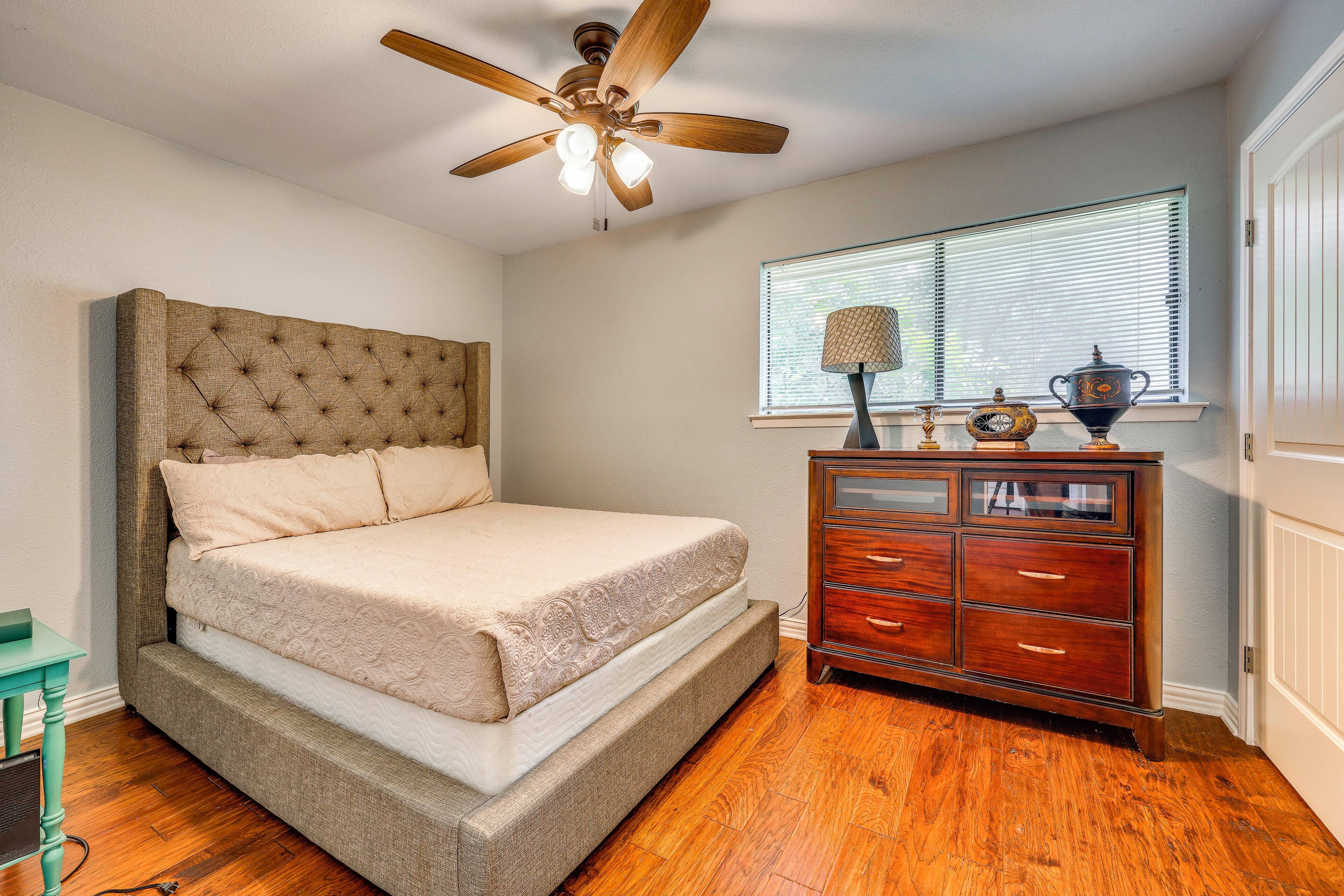 A bedroom with a bed, a dresser, a ceiling fan, and a window with blinds.