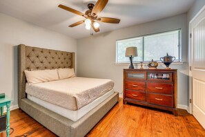 Een slaapkamer met een bed, een dressoir, een plafondventilator en een raam met jaloezieën.