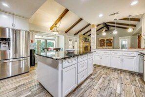A spacious kitchen with white cabinetry, a stainless steel refrigerator, and a large island with a sink. - Luxe Hill Country Home w/ Resort-style Pool! (Buda)