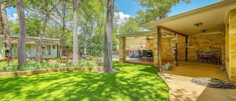 A well-maintained backyard with a lawn, trees, a patio area with outdoor furniture, and a stone building.