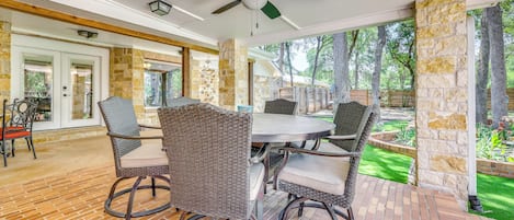 A covered patio area with a round table and wicker chairs, stone walls, and a view of the outdoors.