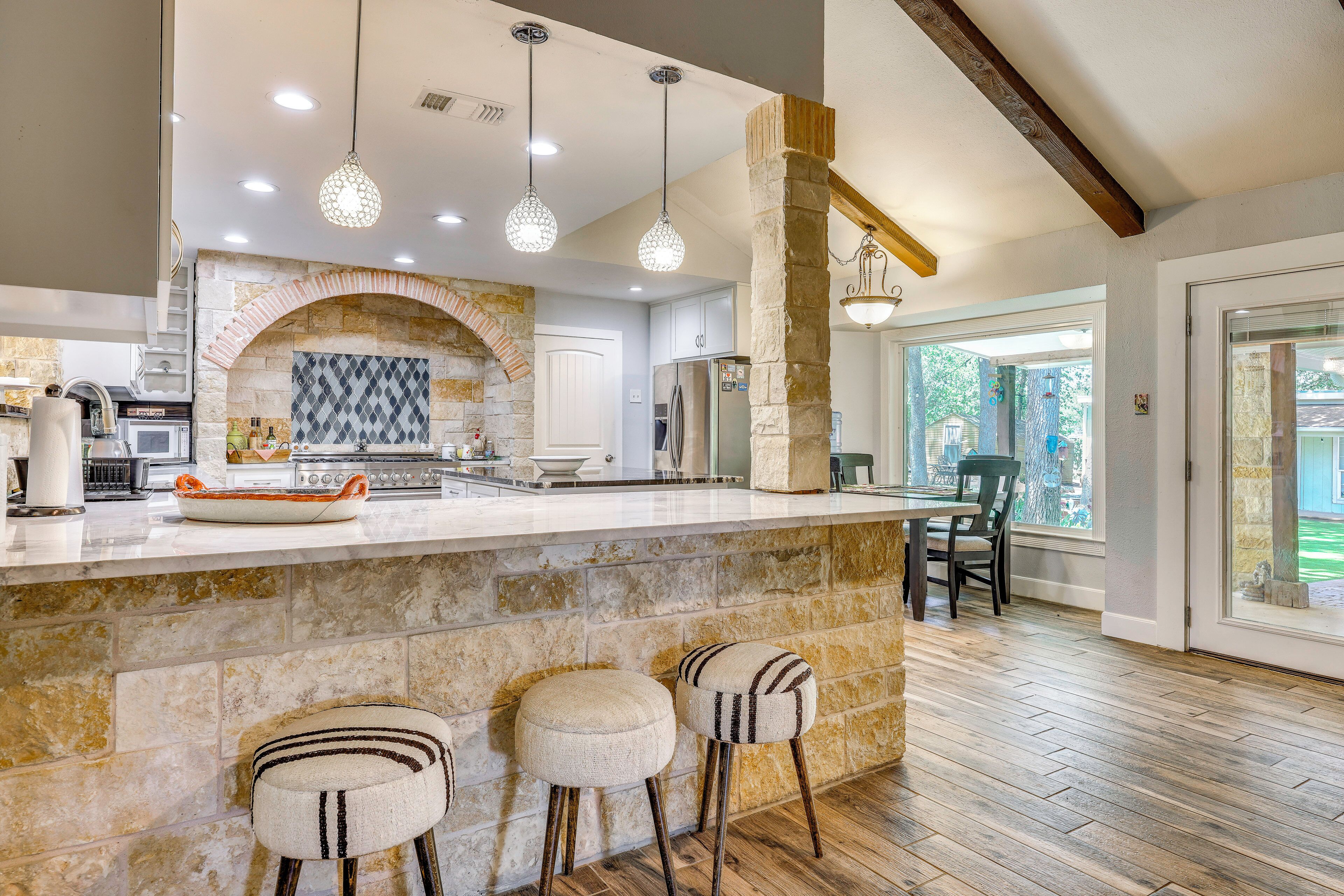 A kitchen with a stone arch, modern appliances, and a bar area with stools.