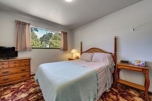 A bedroom with a bed, a dresser, a TV, a window with curtains, and a bedside table with a lamp. - Private Yard & Patio! Pet-friendly Lynnwood Home (Lynnwood)
