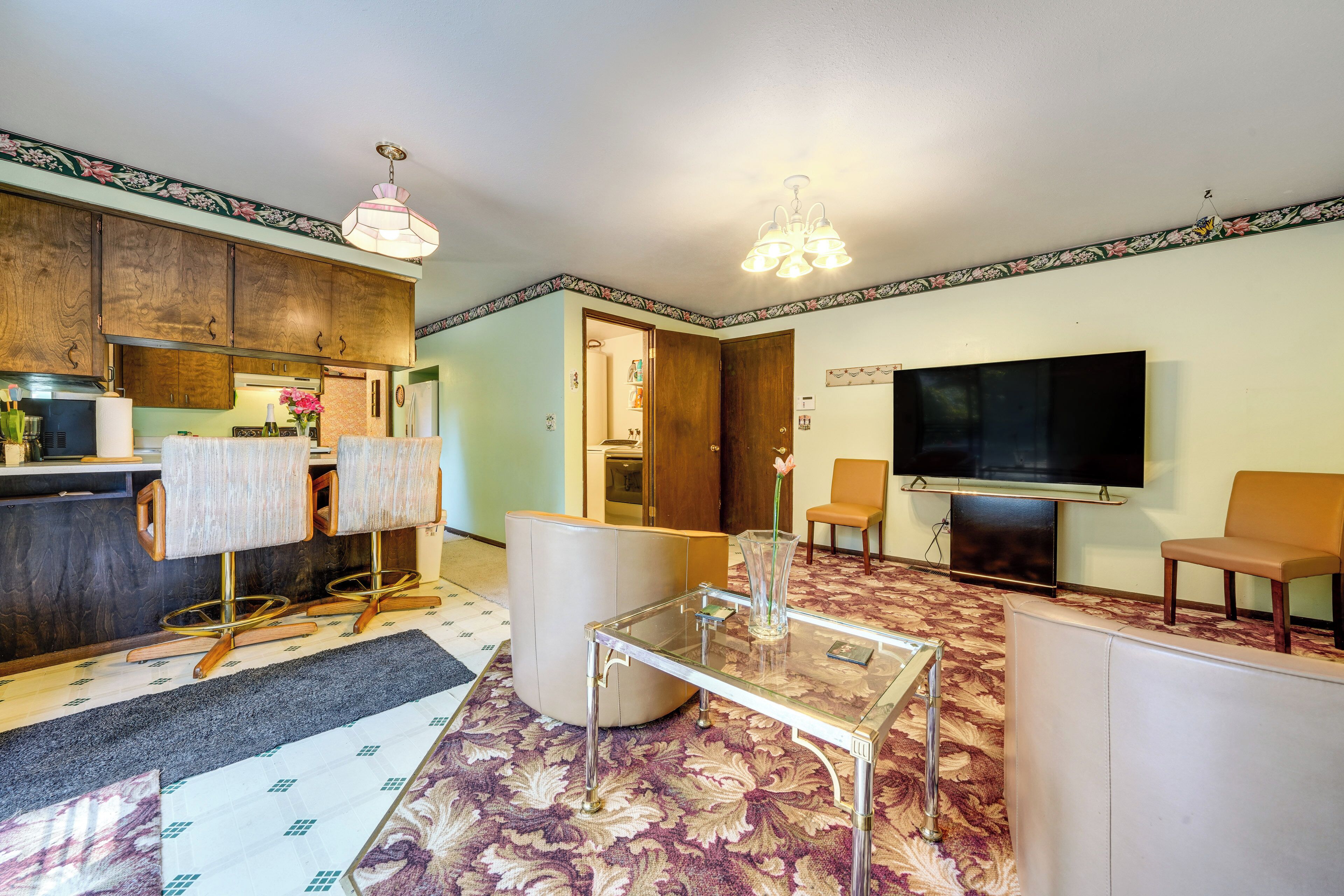 A living room with a TV, seating, a coffee table, and a kitchen area.