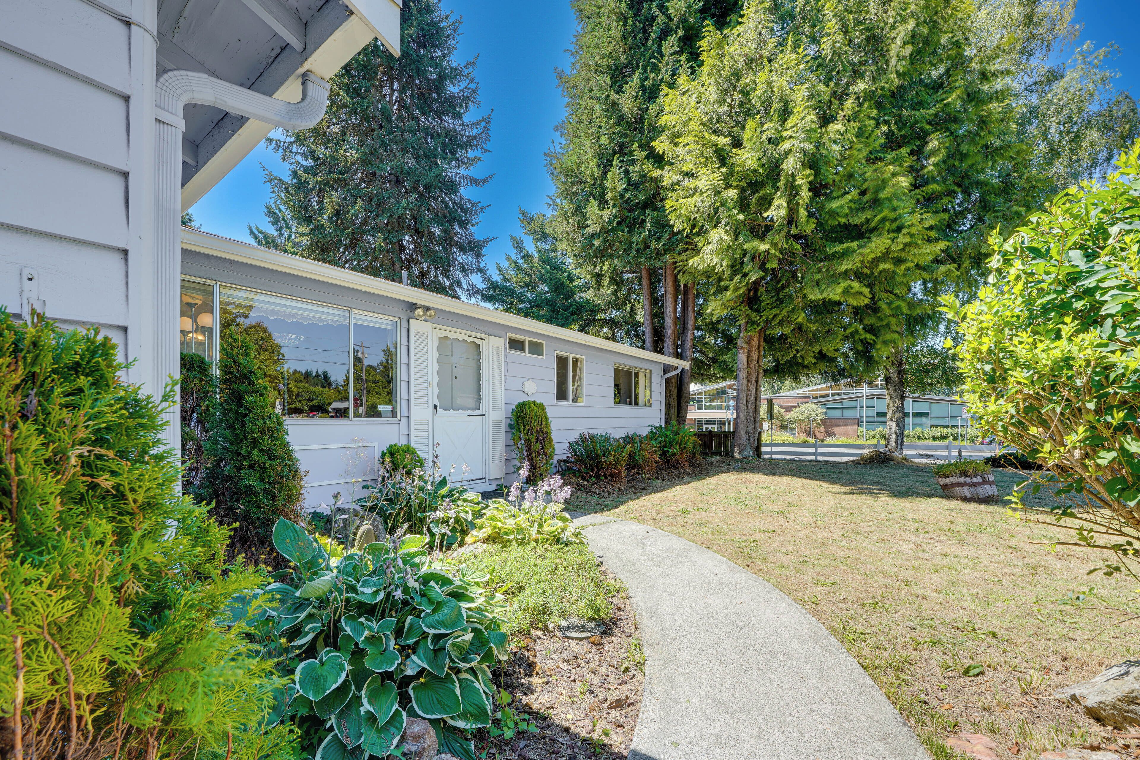 A single-story house with a covered porch, surrounded by lush greenery and a clear sky.