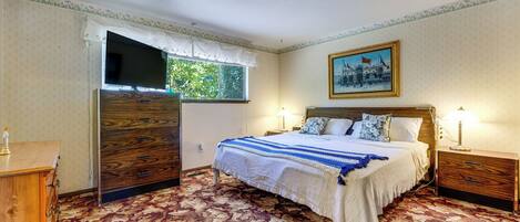 A bedroom with a bed, a nightstand, a dresser, a television, and a window.