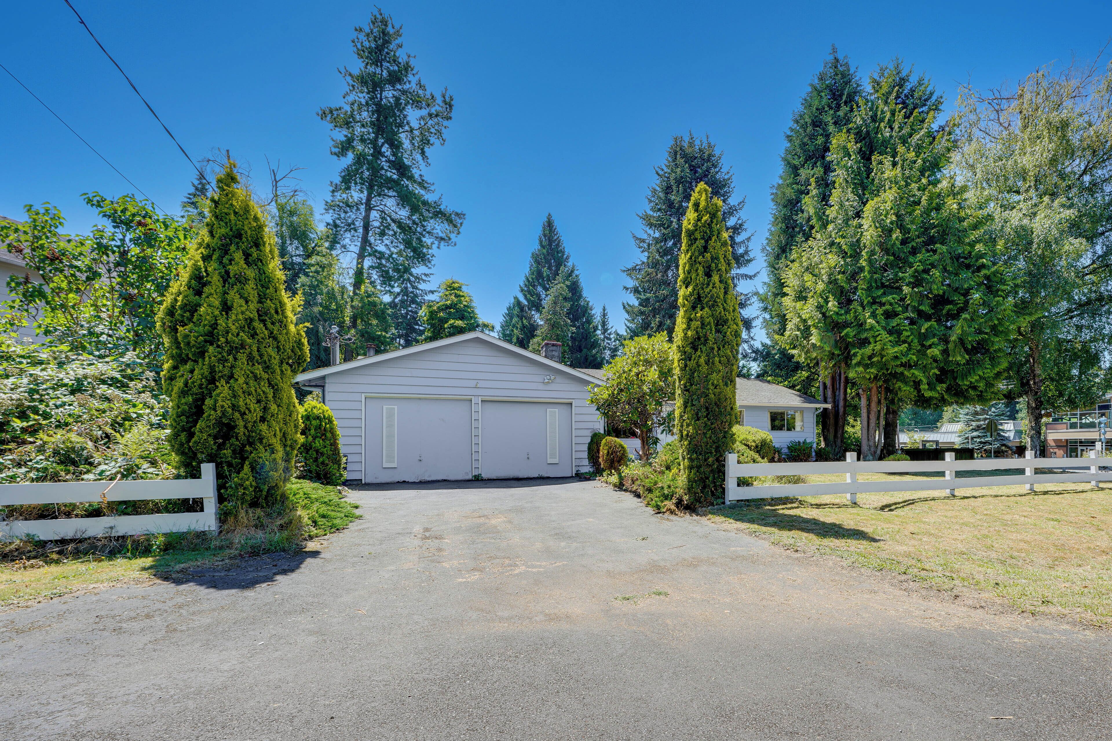 A residential driveway leading to a garage with a white fence on either side.