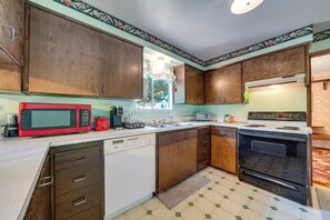 A compact kitchen with wooden cabinets, a red microwave, a toaster, a kettle, and a stove. - Private Yard & Patio! Pet-friendly Lynnwood Home (Lynnwood)