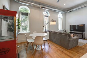 A modern living room with a dining area, large windows, and a flat-screen TV. - Walkable & Stylish! Cincy Loft in Prime OTR Spot (Cincinnati)