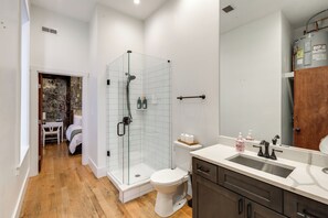 A modern bathroom with a glass shower enclosure, a white toilet, and a wooden floor. - Walkable & Stylish! Cincy Loft in Prime OTR Spot (Cincinnati)