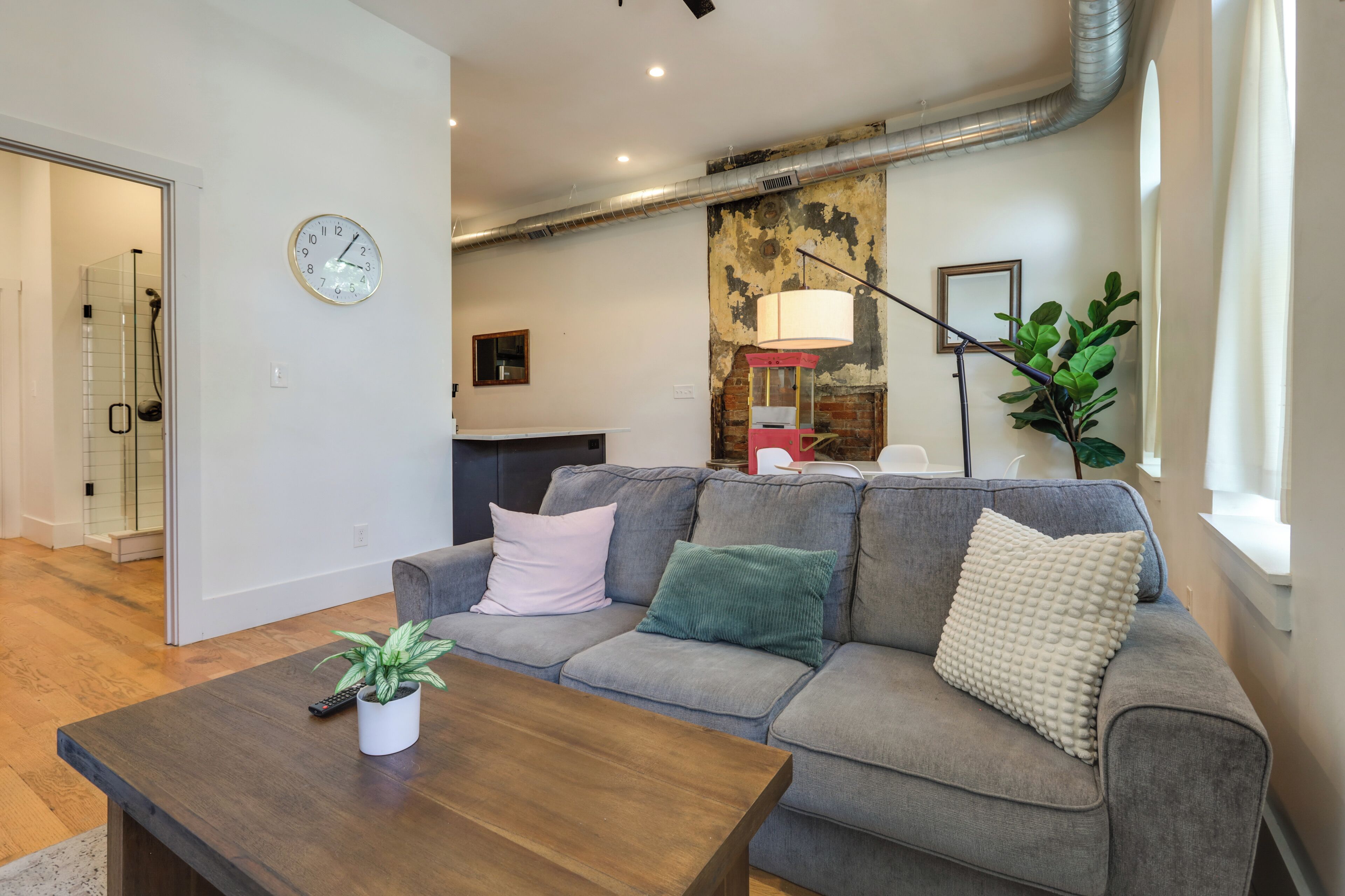 Uma sala de estar moderna com um sofá cinzento, uma mesa de centro de madeira e uma planta em vaso.