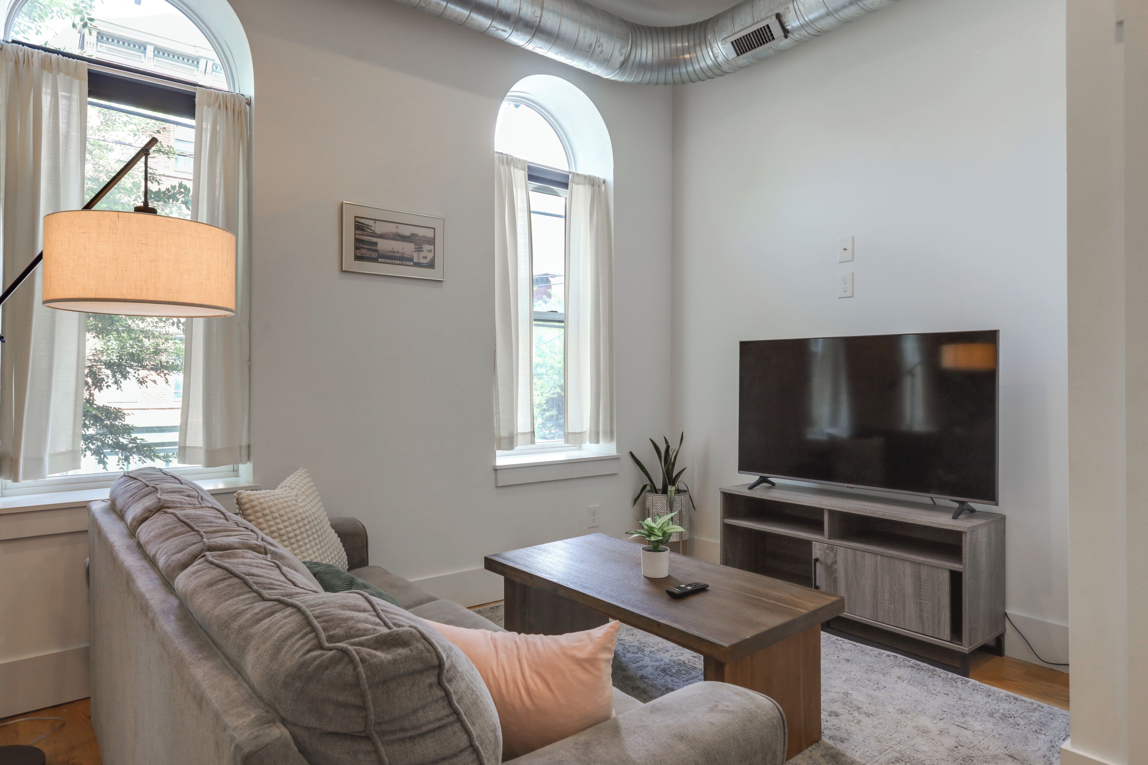 A modern living room with a sectional sofa, a flat-screen TV, and a large window with a view of trees.