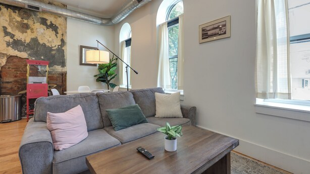 Een moderne woonkamer met een grijze bank, een houten salontafel en een plant in pot.