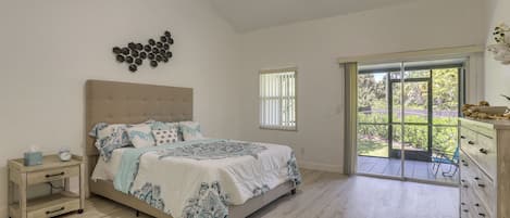 A bedroom with a bed, bedside table, and a view of the outdoors through a sliding door.