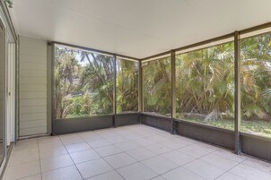 Une pièce dotée de grandes fenêtres, d’un sol carrelé et offrant une vue sur la végétation tropicale.